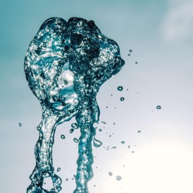 Close-up of water splash in mid-air against a bright sky, capturing motion and transparency.